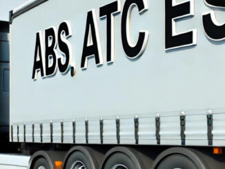 A commercial truck with a trailer on a clear highway, showing the abbreviations ABS, ATC, and ESP visibly printed on the side of the trailer.