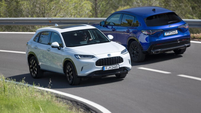 Ein weißer und blauer Honda ZR-V fahren 2023 auf einer Landstraße aneinander vorbei.